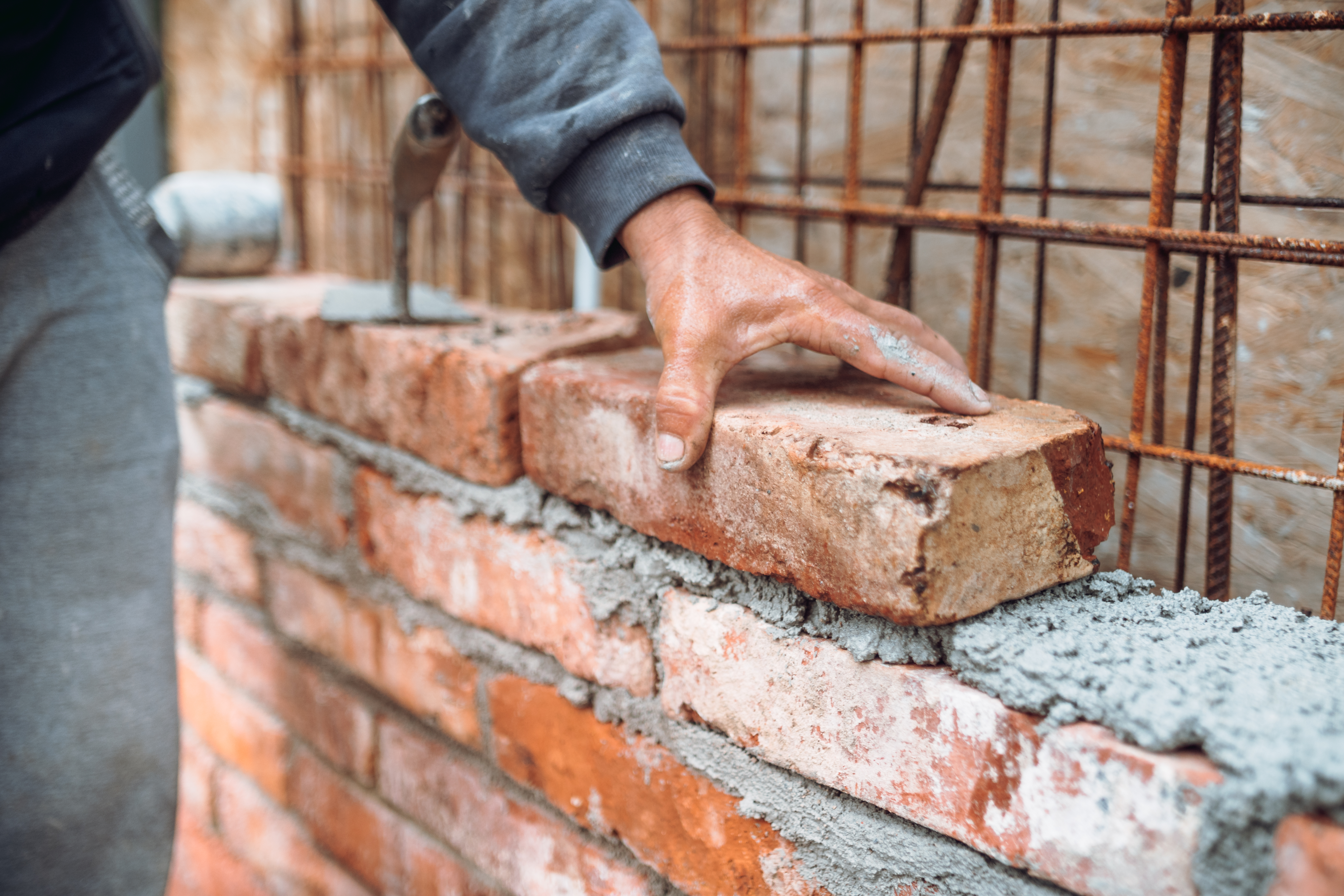 Bricklayer placing and adjusting bricks with mortar.