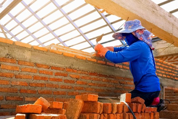 Female construction worker working to build brick wall inside of house construction site